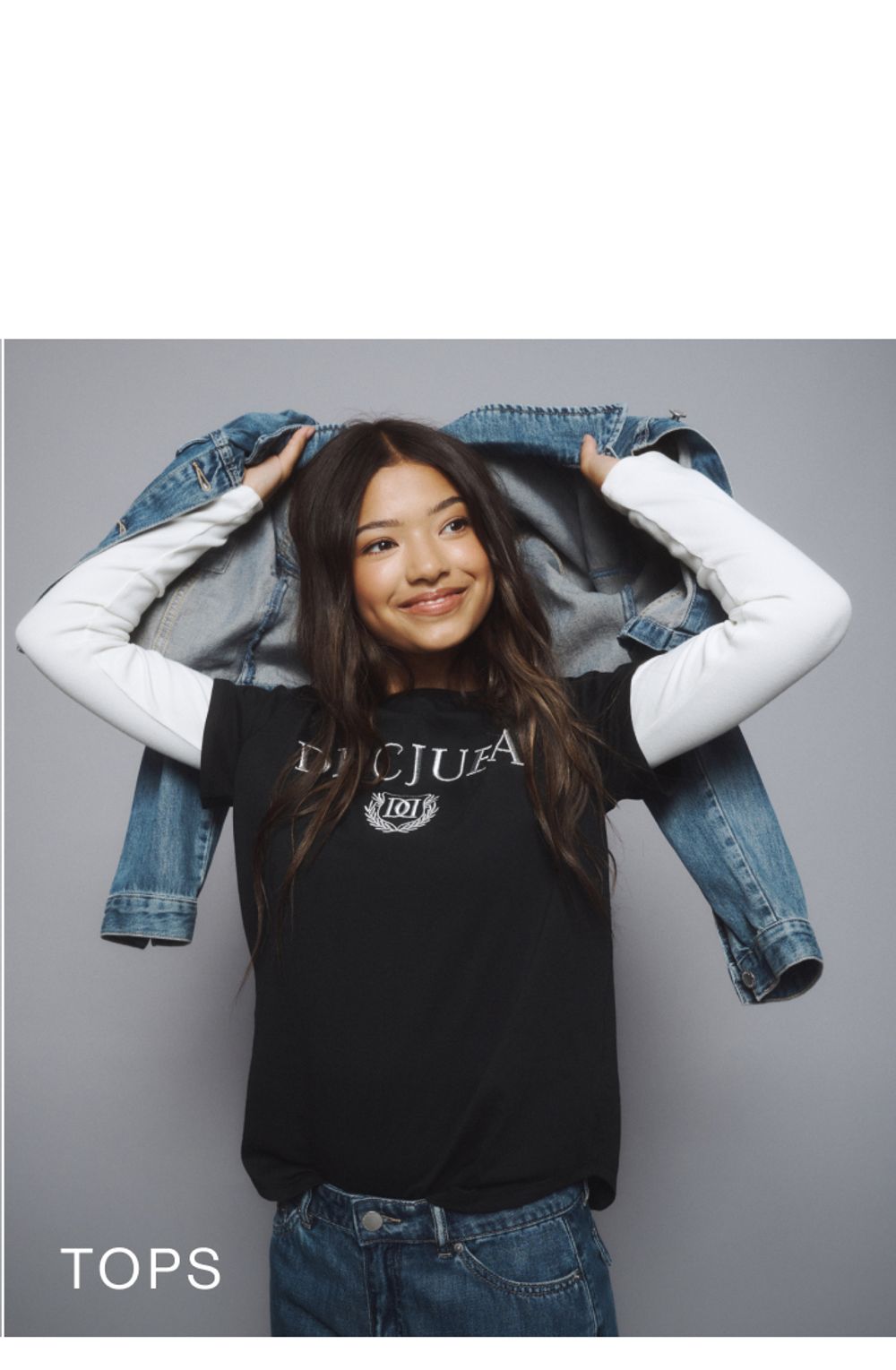 Young girl wearing a black Decjuba tee layered over a white long sleeve top. SHOP TEEN TOPS.