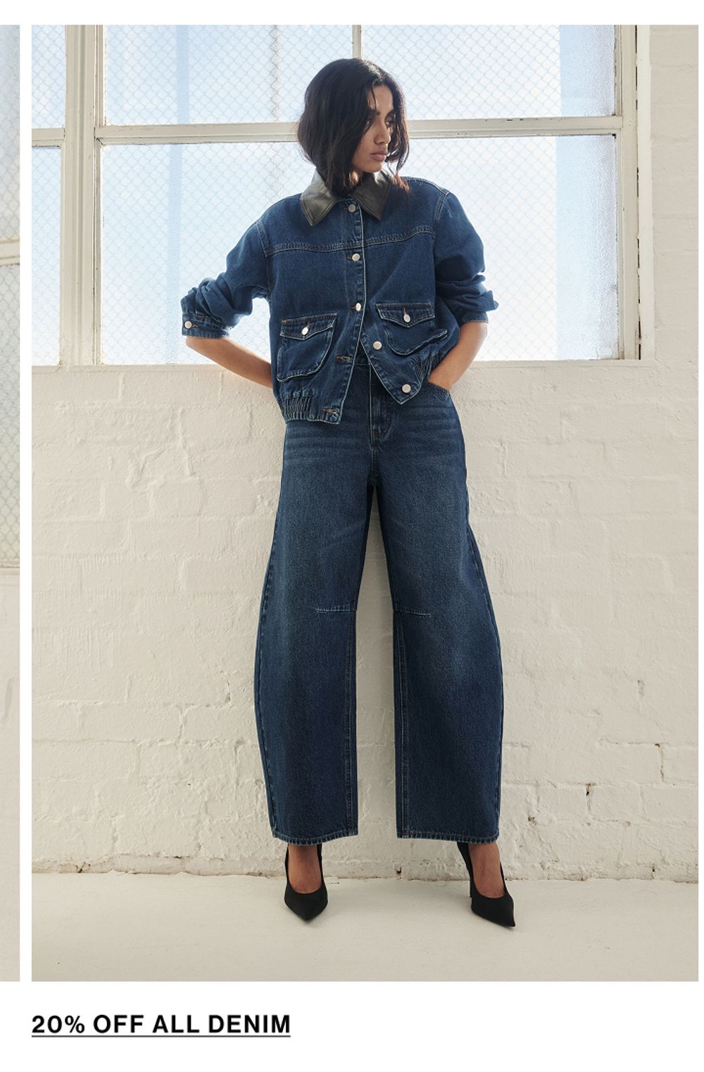 Model posing in a blue denim set in a studio. SHOP DENIM.