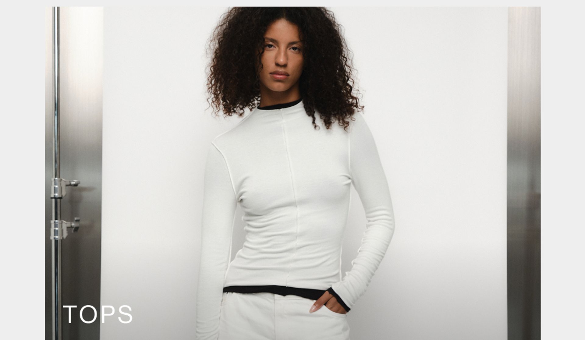 Model wearing a white long sleeve top layered over a black long sleeve top. SHOP D-LUXE TOPS.