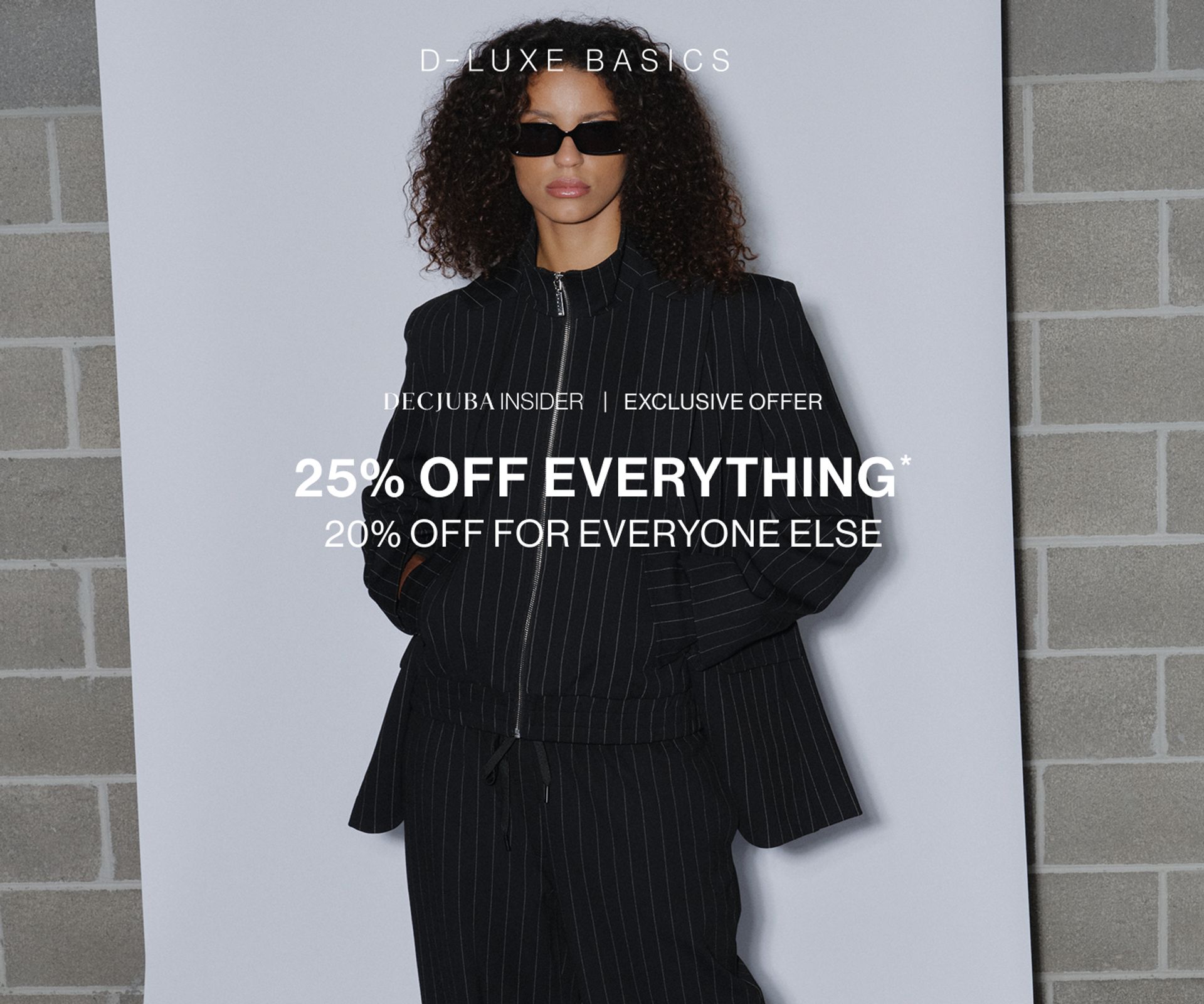 Model wearing black pinstripe suit against a neutral background. SHOP NEW 25% OFF D-LUXE.