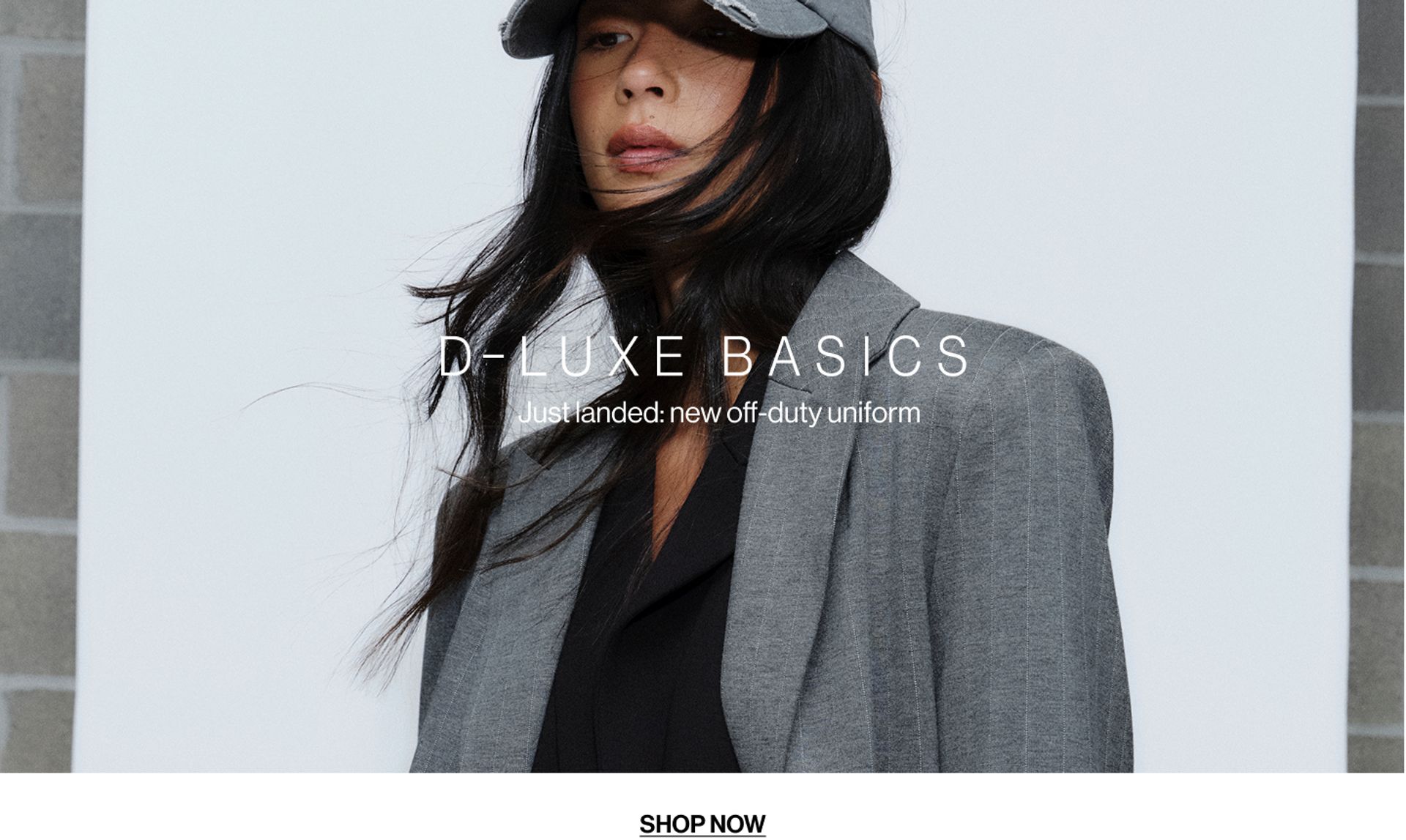 Model wearing a charcoal blazer coat in a studio. Text reads D-LUXE BASICS