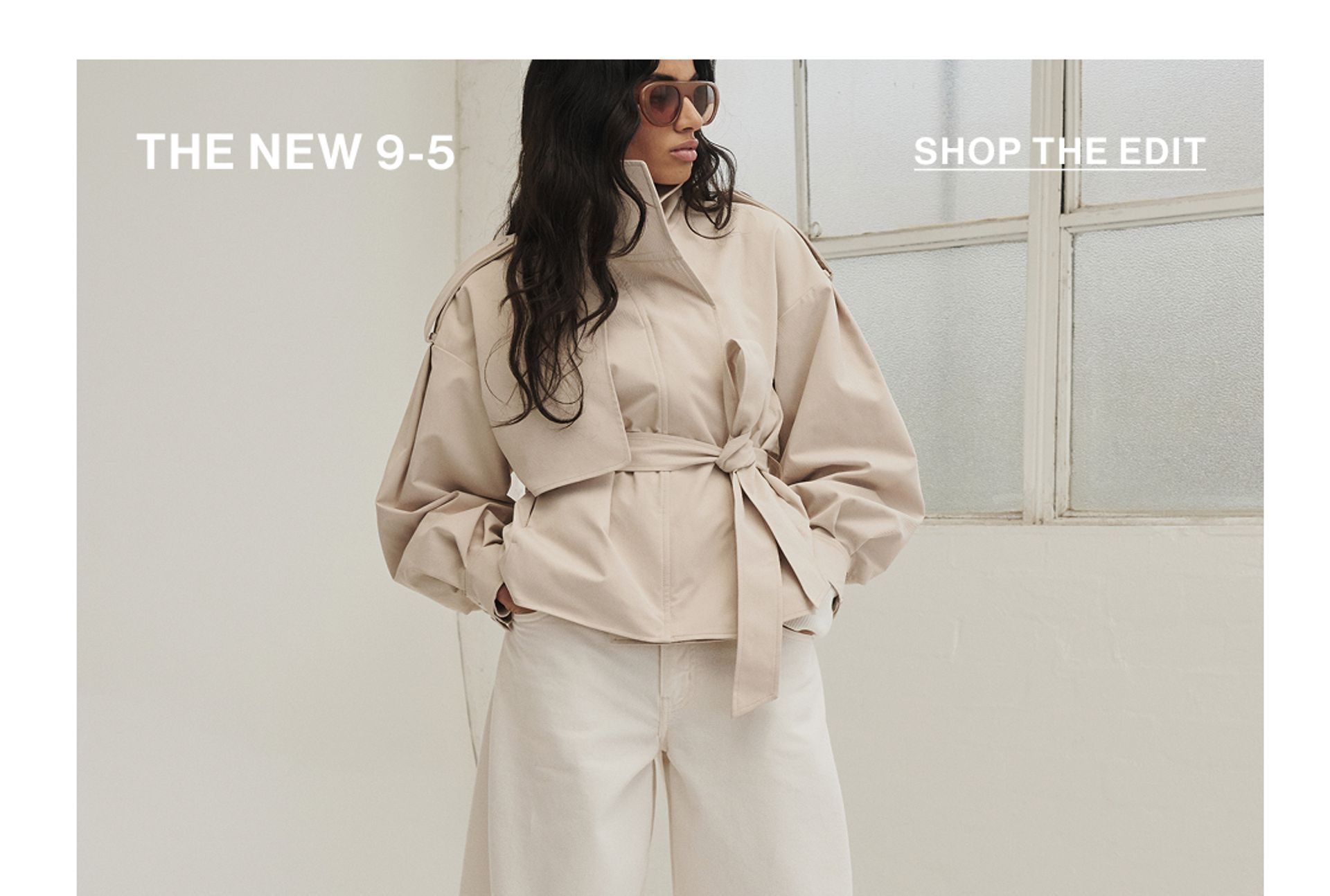 Model standing with hand in her pockets wearing an almond cropped trench jacket with text overlay: "THE NEW 9-5""