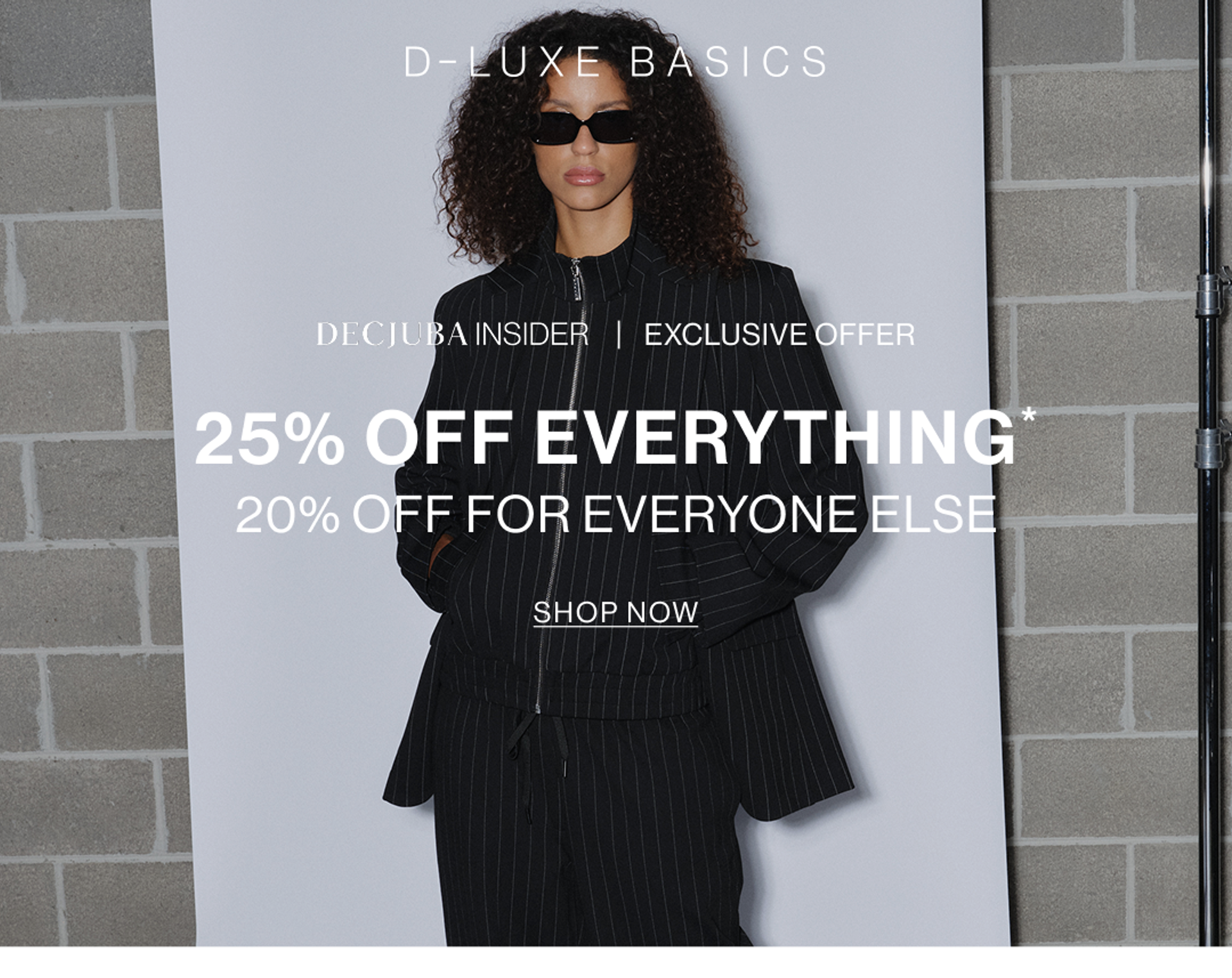 Model wearing black pinstripe suit against a neutral background. SHOP NEW 25% OFF D-LUXE.