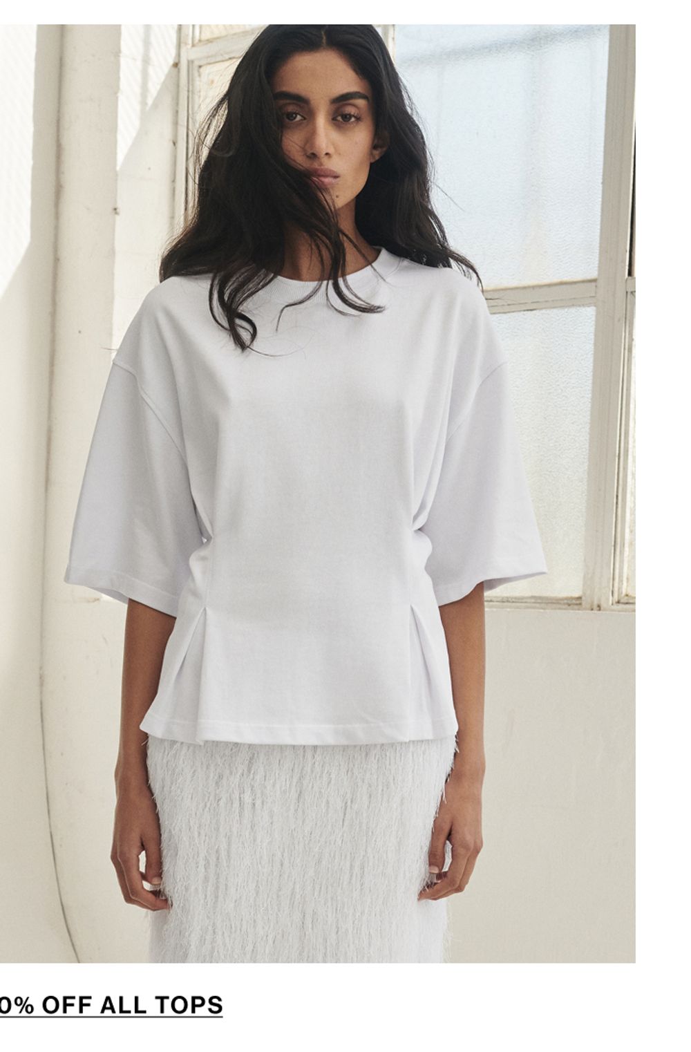 Model posing wearing a white tee. SHOP TOPS.