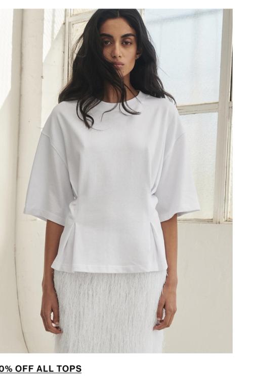 Model posing wearing a white tee. SHOP TOPS.