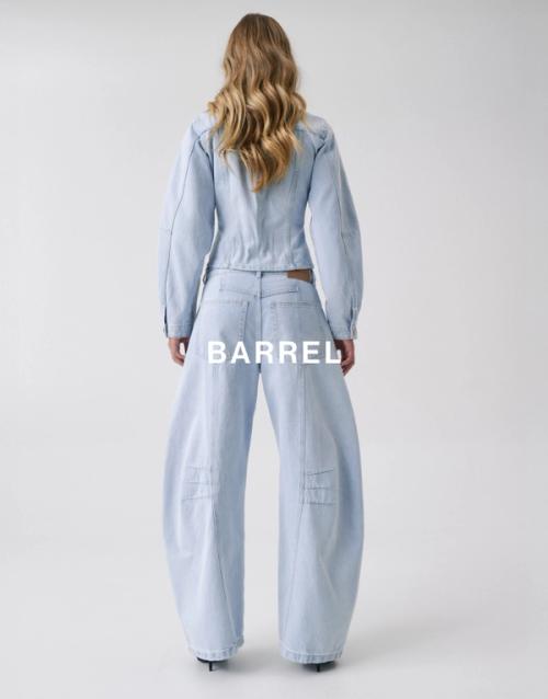 Back view of Jess Hart wearing light blue barrel-leg jeans and matching denim top. SHOP BARREL JEANS.