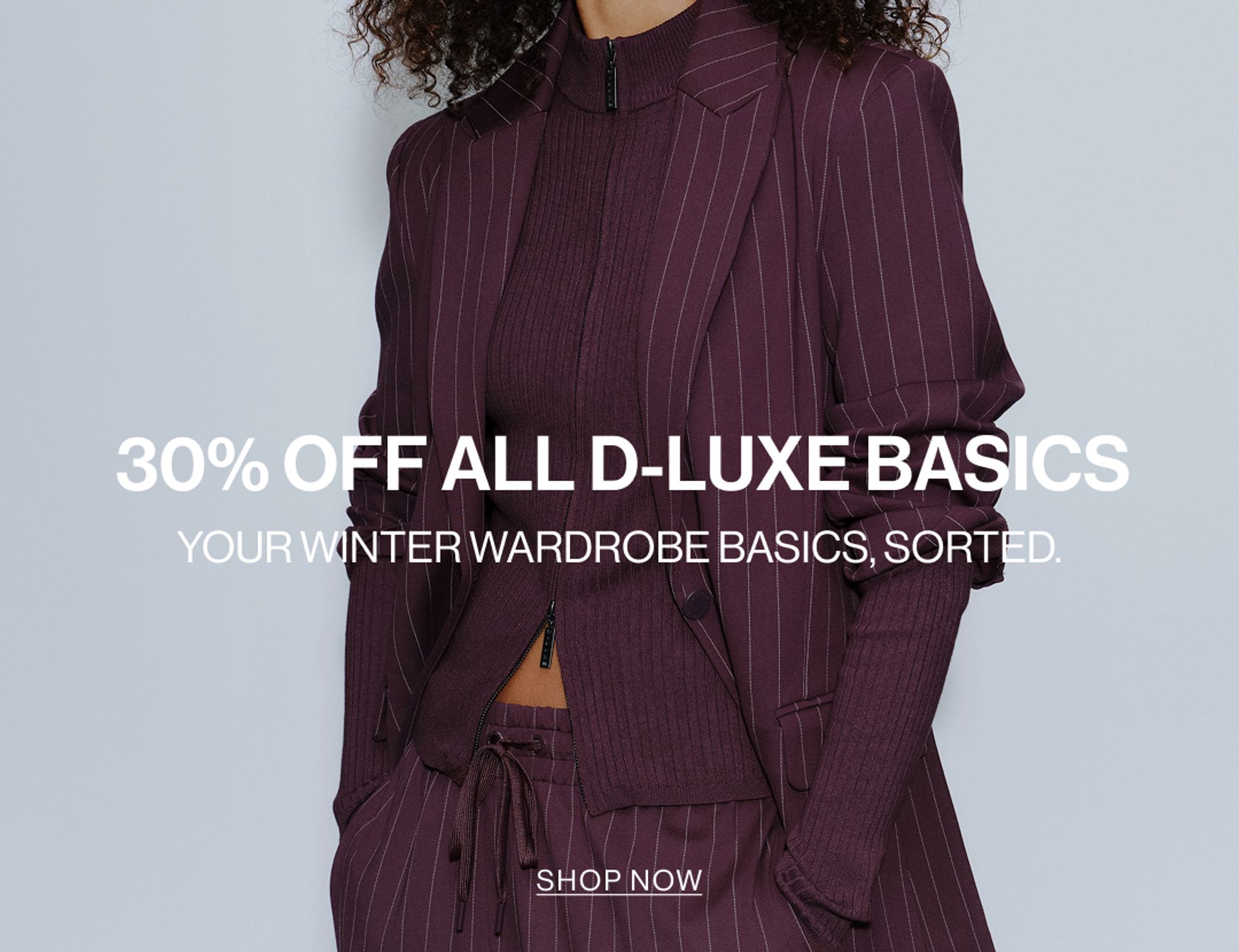 Model wearing a pinstripe blazer and pants in midnight cherry in a studio. SHOP NEW D-LUXE.
