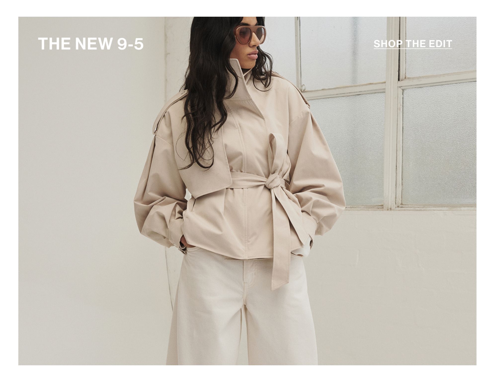 Model standing with hand in her pockets wearing an almond cropped trench jacket with text overlay: "THE NEW 9-5""