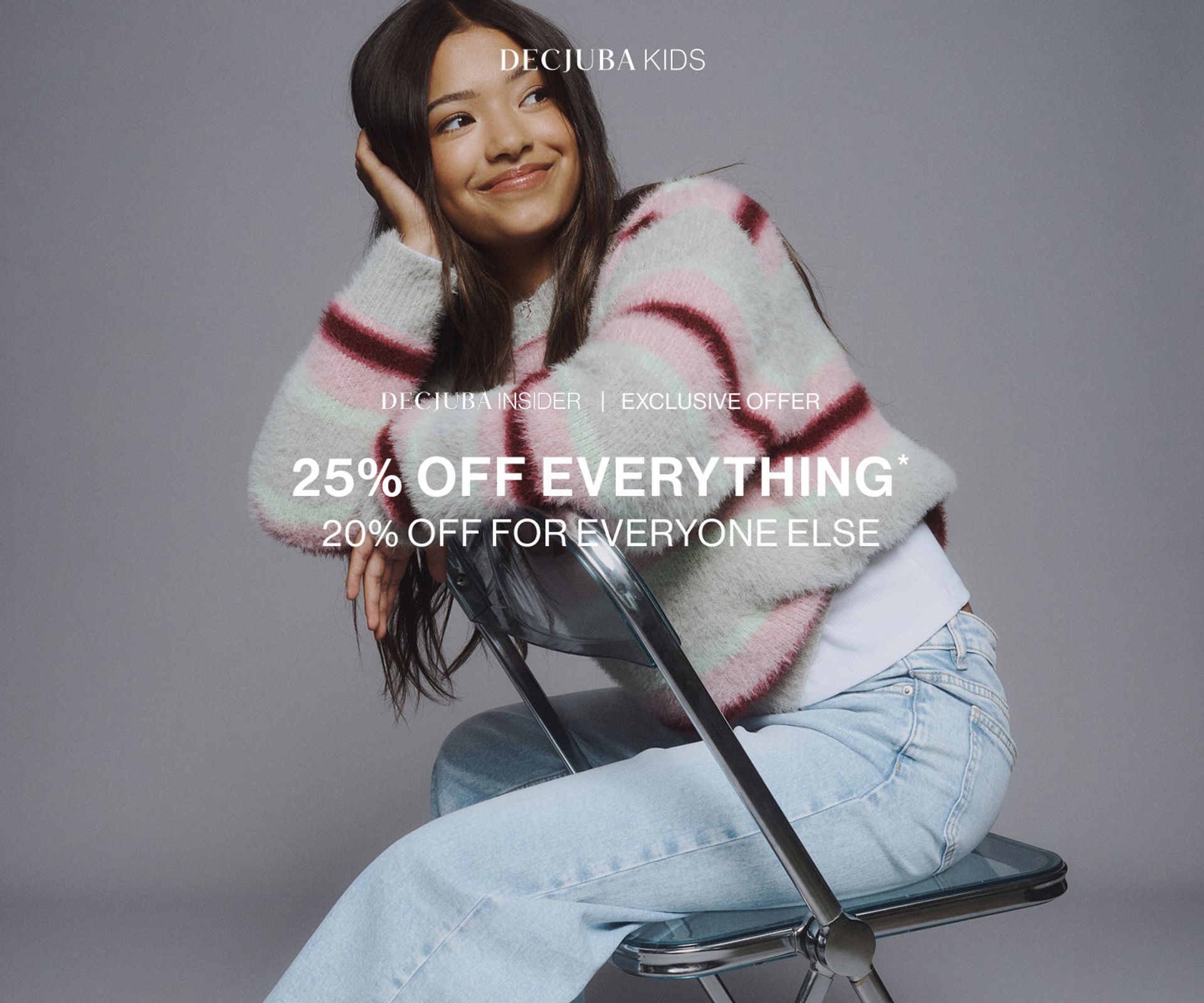 Young model wearing a striped knit with light blue jeans sitting on a chair. SHOP 25% OFF KIDS.
