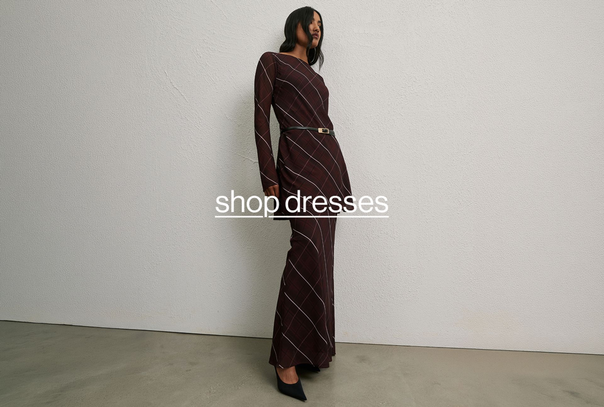 Model in a check print burgundy dress standing against a neutral background.