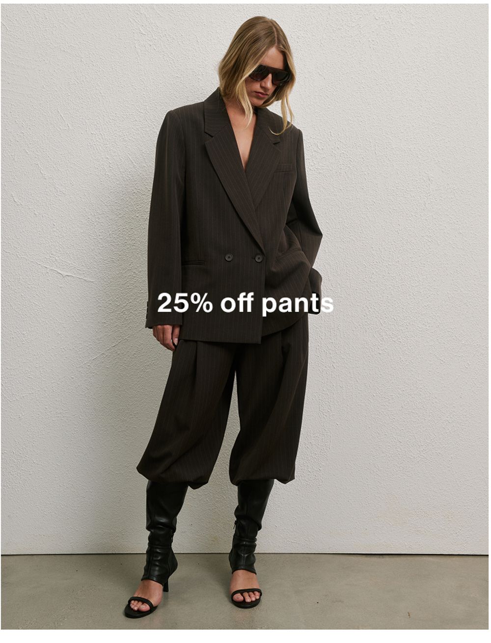 Woman in chocolate pinstripe set against a neutral background, promoting 25% off pants.