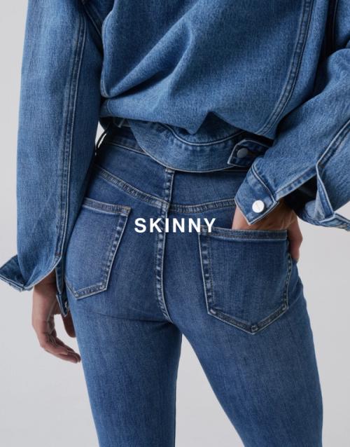 Close-up back view of Jess Hart wearing mid-wash skinny jeans with a hand in the back pocket and a denim shirt layered over top. SHOP SKINNY JEANS.