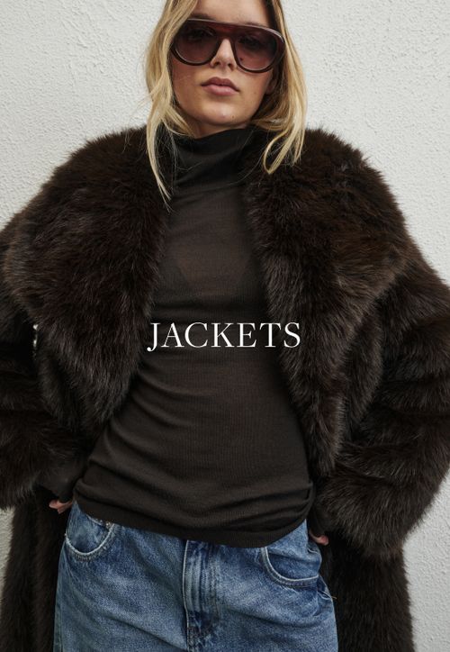 Model wearing a brown faux fur jacket. SHOP JACKETS.