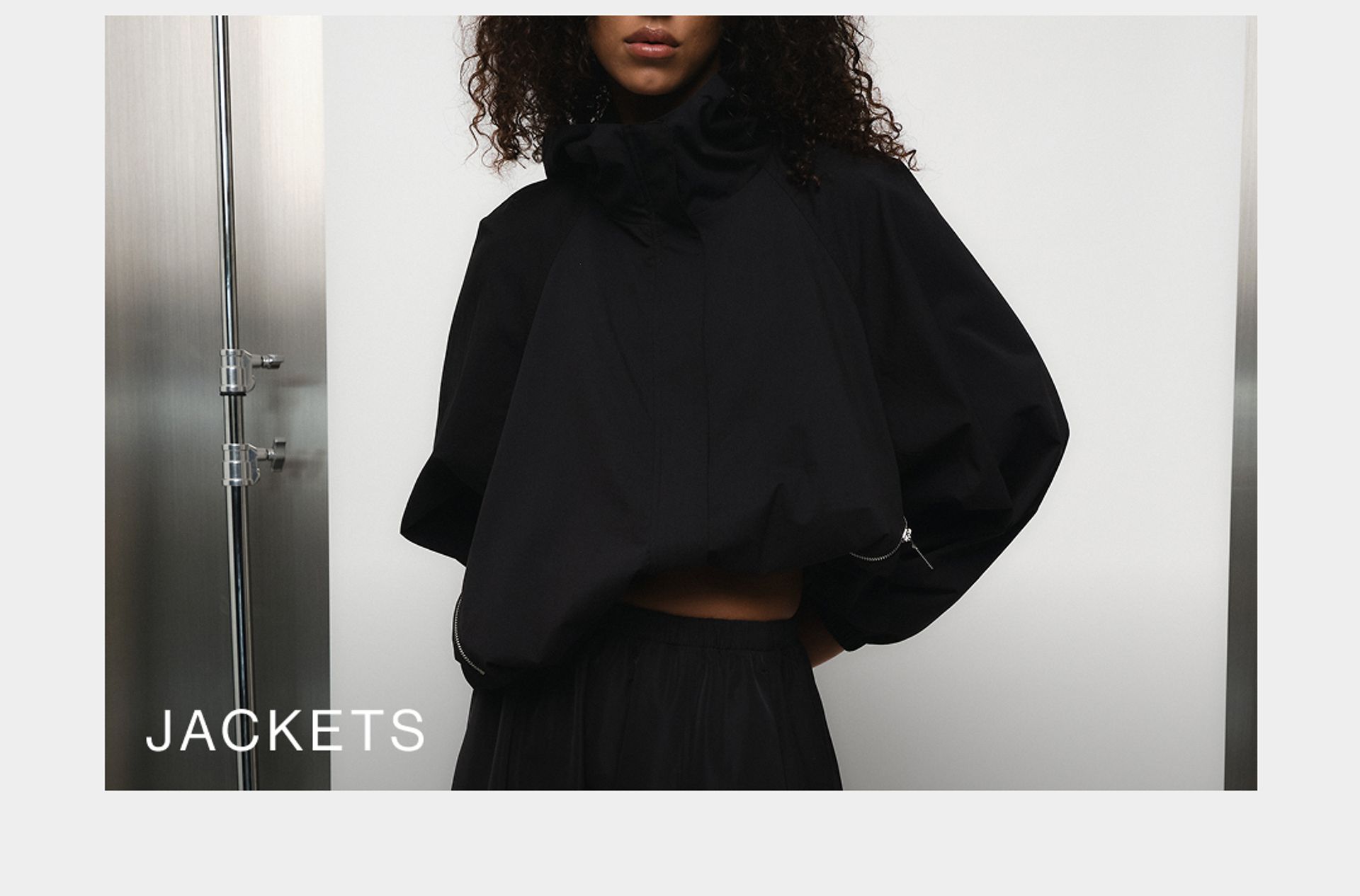 Model wearing a black high neck jacket against a neutral background. SHOP D-LUXE JACKETS.