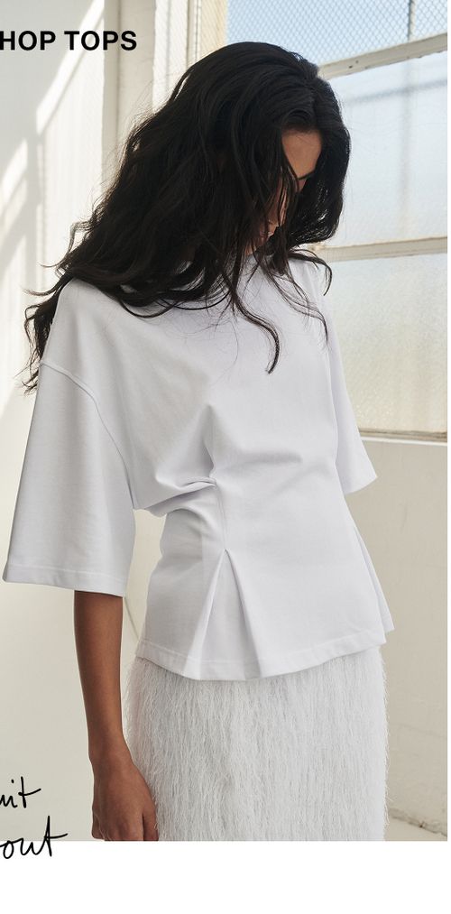 Model posing wearing a white tee. SHOP TOPS.