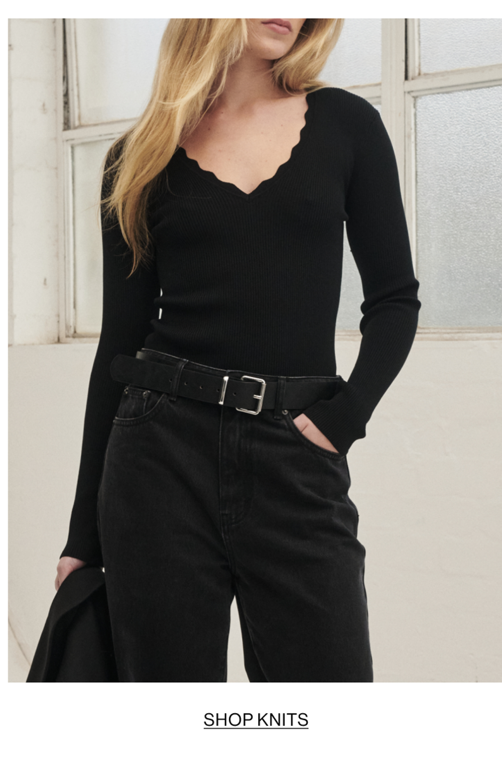 Model posing in a knit v neck top in black. SHOP KNITS.