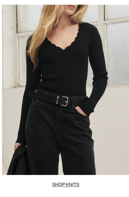 Model posing in a knit v neck top in black. SHOP KNITS.