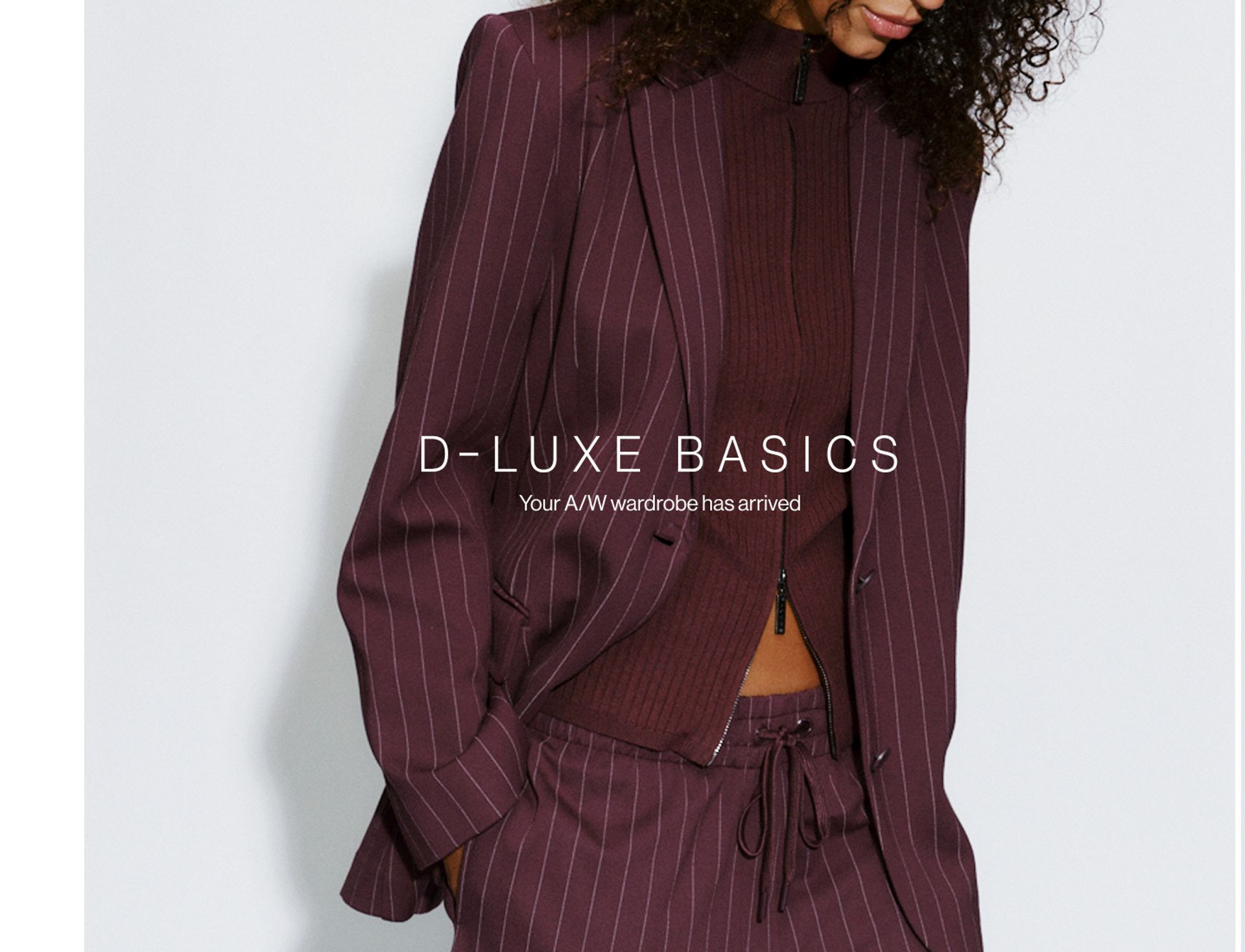 Model wearing a pinstripe blazer and pants in midnight cherry in a studio. SHOP NEW D-LUXE.
