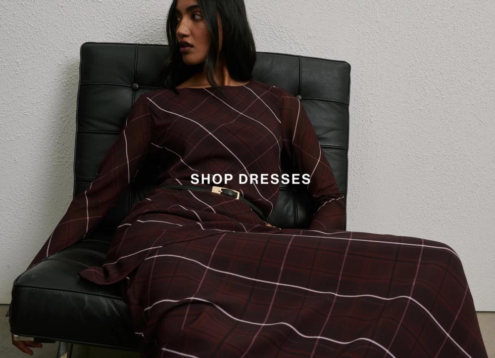 Model seated in a burgundy long-sleeve midi dress with subtle grid pattern – Shop Dresses.