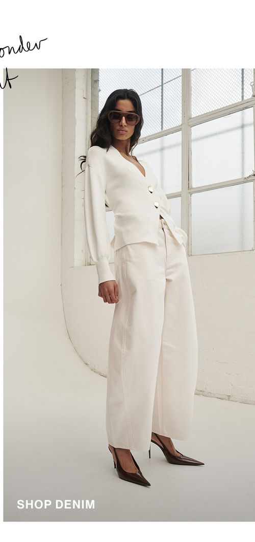 Model posing in a pair of white denim jeans in a studio. SHOP DENIM.