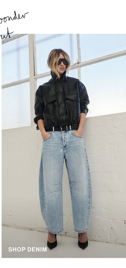 Model posing in a pair of light blue denim jeans in a studio. SHOP DENIM.