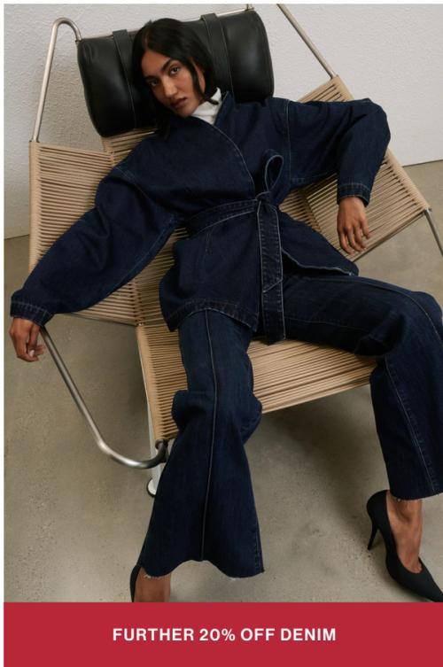 Model sitting in a chair in a dark denim set. SHOP FURTHER 20% OFF SALE DENIM.