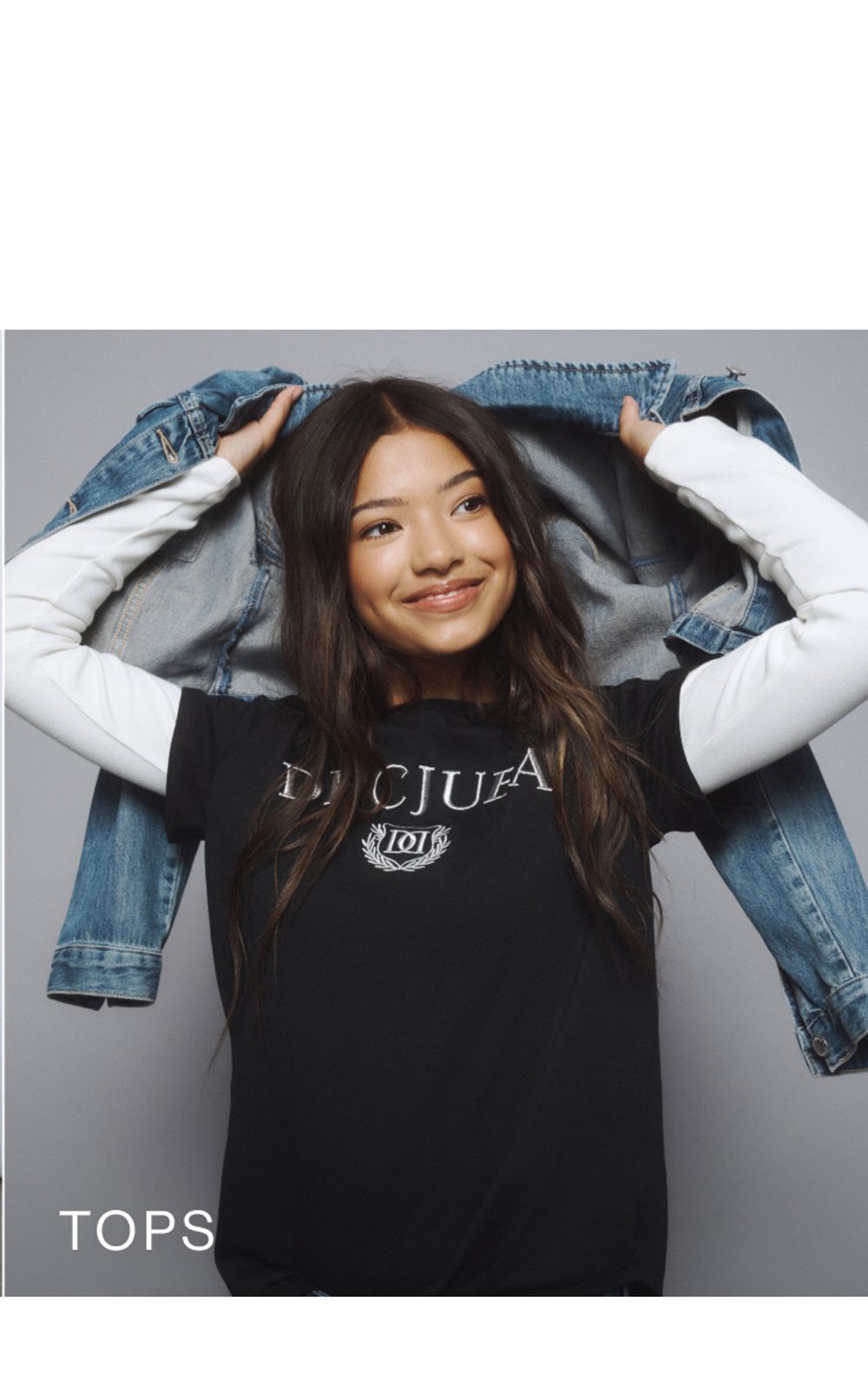Young girl wearing a black Decjuba tee layered over a white long sleeve top. SHOP TEEN TOPS.