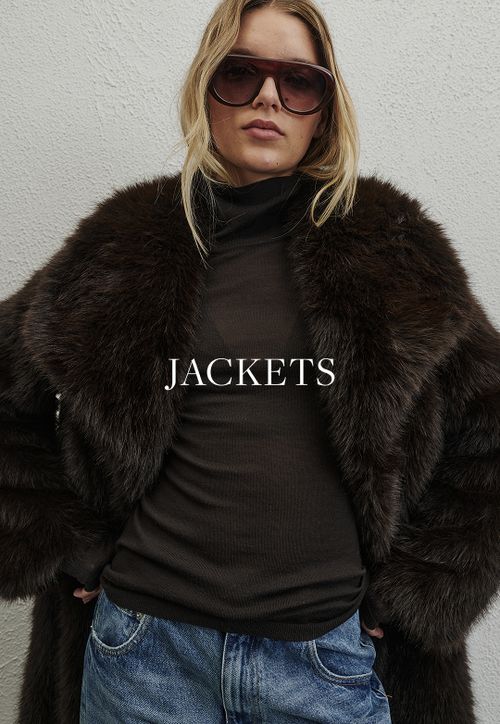 Model wearing a brown faux fur jacket. SHOP JACKETS.