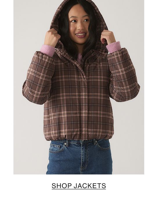 Young model wearing a brown and pink gingham pattern puffer jacket. SHOP TEEN GIRL JACKETS.