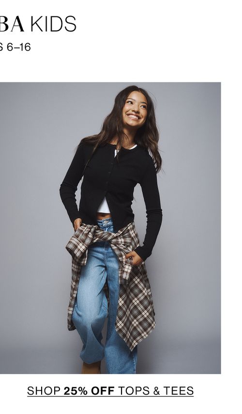 Young girl sitting cross-legged wearing a denim jacket, jeans, and sneakers