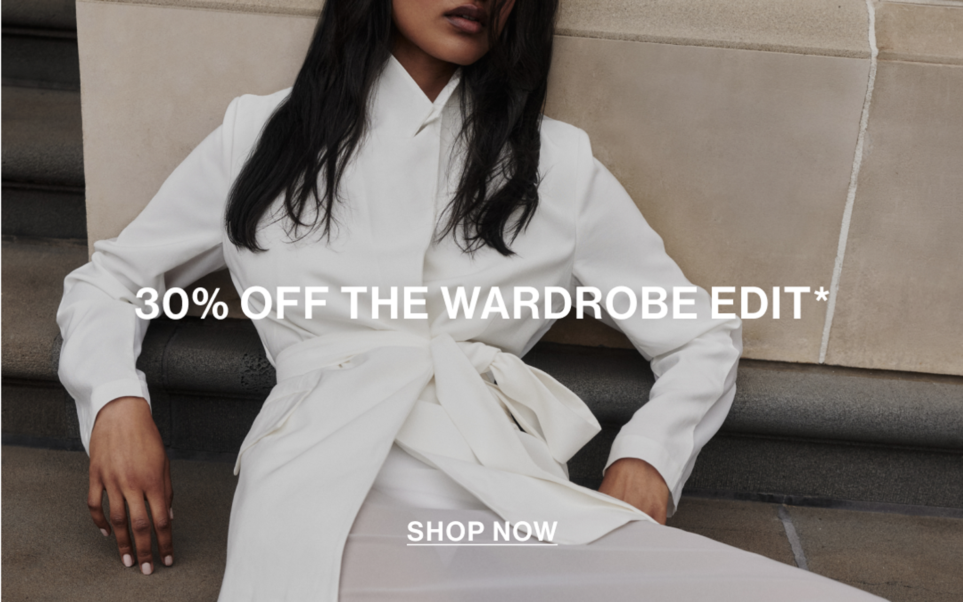 Model lying down against a wall wearing a white organza blazer and skirt with text overlay: "30% OFF THE WARDROBE EDIT."