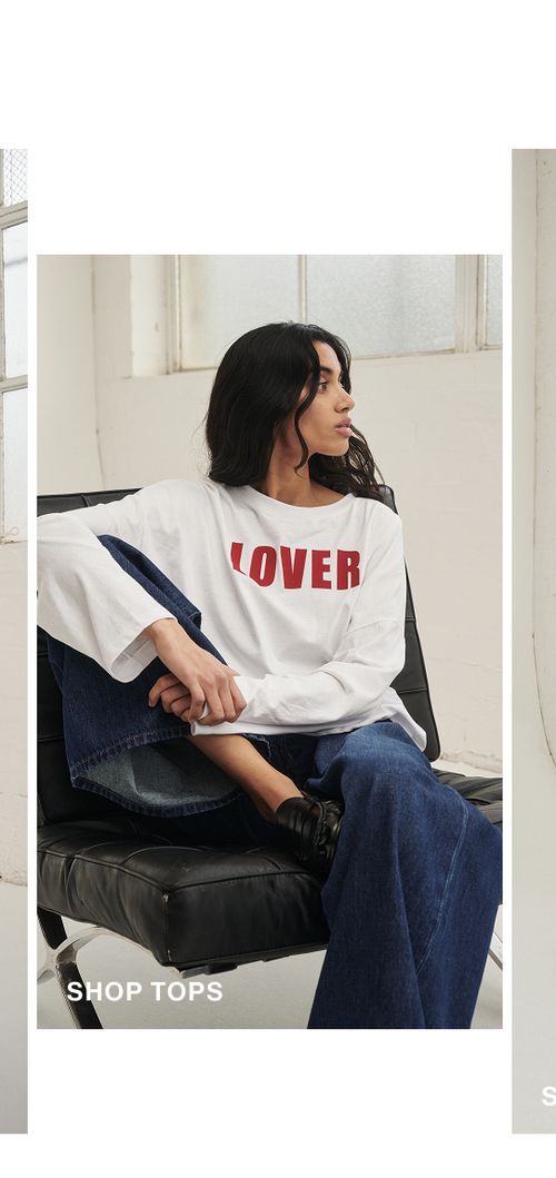 Model posing wearing a white long sleeve tee with 'LOVER' written on it. SHOP TOPS.