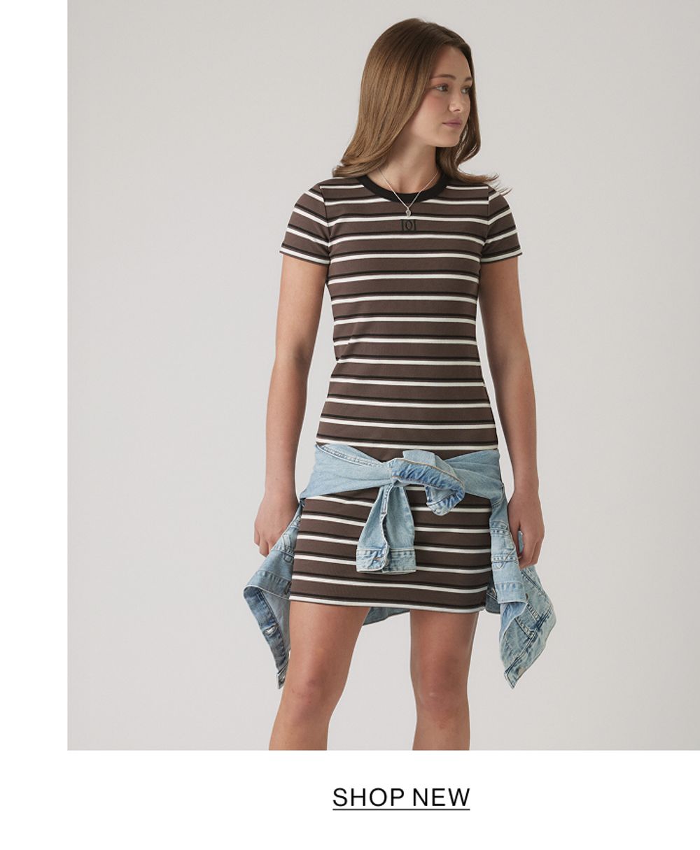 Young girl wearing a brown and cream striped short-sleeve tee with light denim tied around her waist, standing against a neutral background.