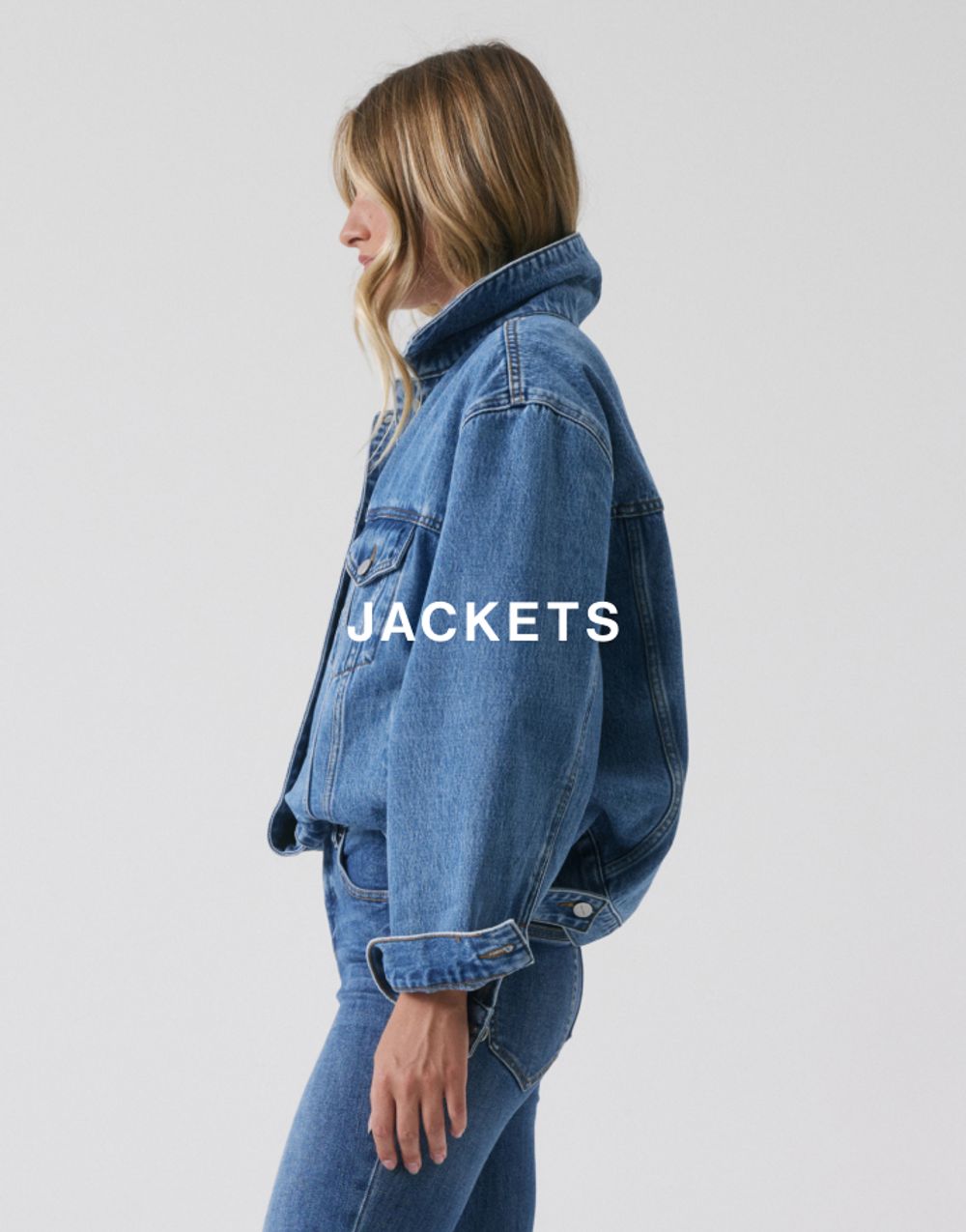 Side profile of model wearing a classic blue denim jacket with a high collar. SHOP DENIM JACKETS.