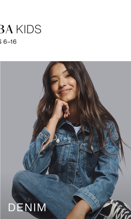 Young girl sitting on a chair with legs crossed wearing a denim set. SHOP TEEN DENIM.