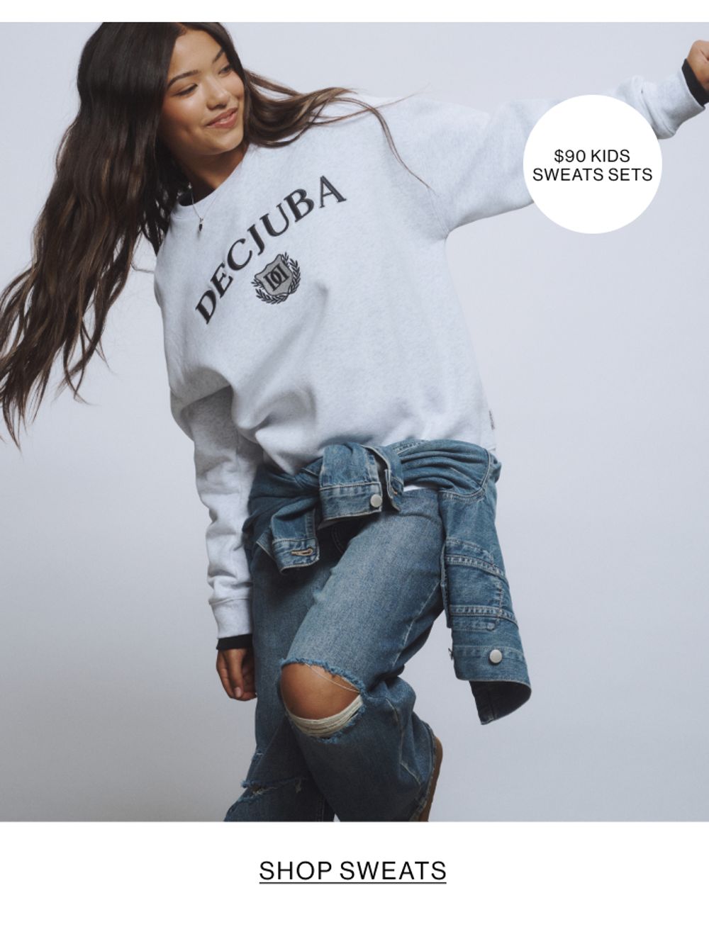 Young girl wearing a grey sweatshirt and ripped jeans with a denim jacket tied at the waist.