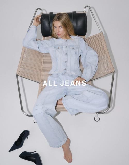 Jess Hart reclining in a chair wearing a light wash denim shirt and wide-leg jeans. SHOP ALL JEANS.