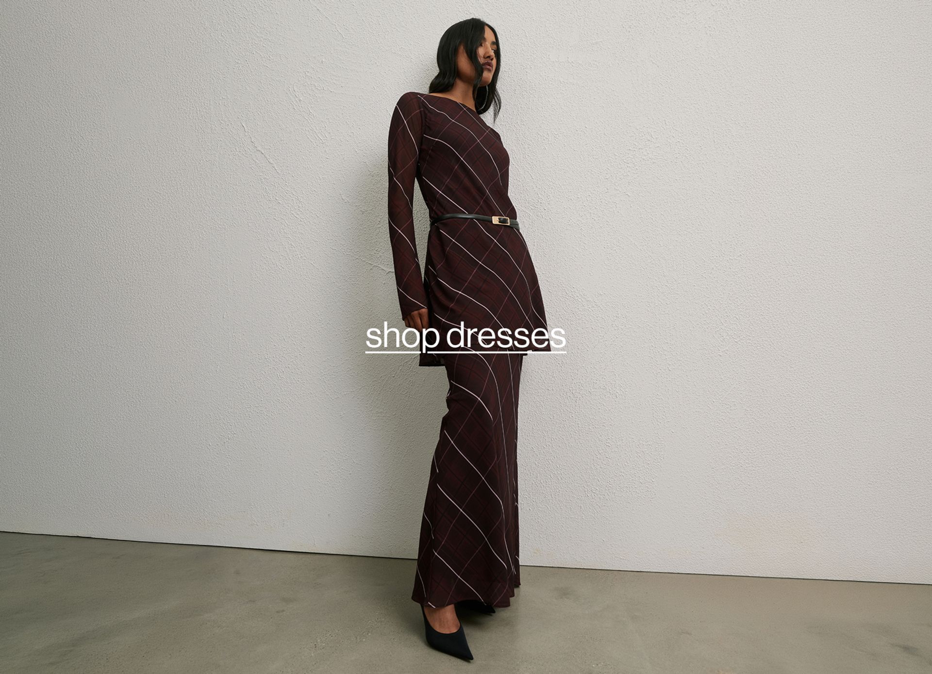 Model in a check print burgundy dress standing against a neutral background.