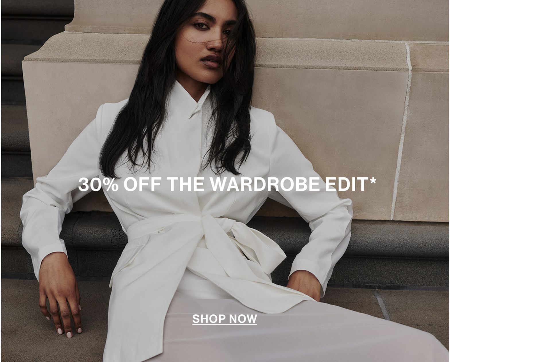 Model lying down against a wall wearing a white organza blazer and skirt with text overlay: "30% OFF THE WARDROBE EDIT."