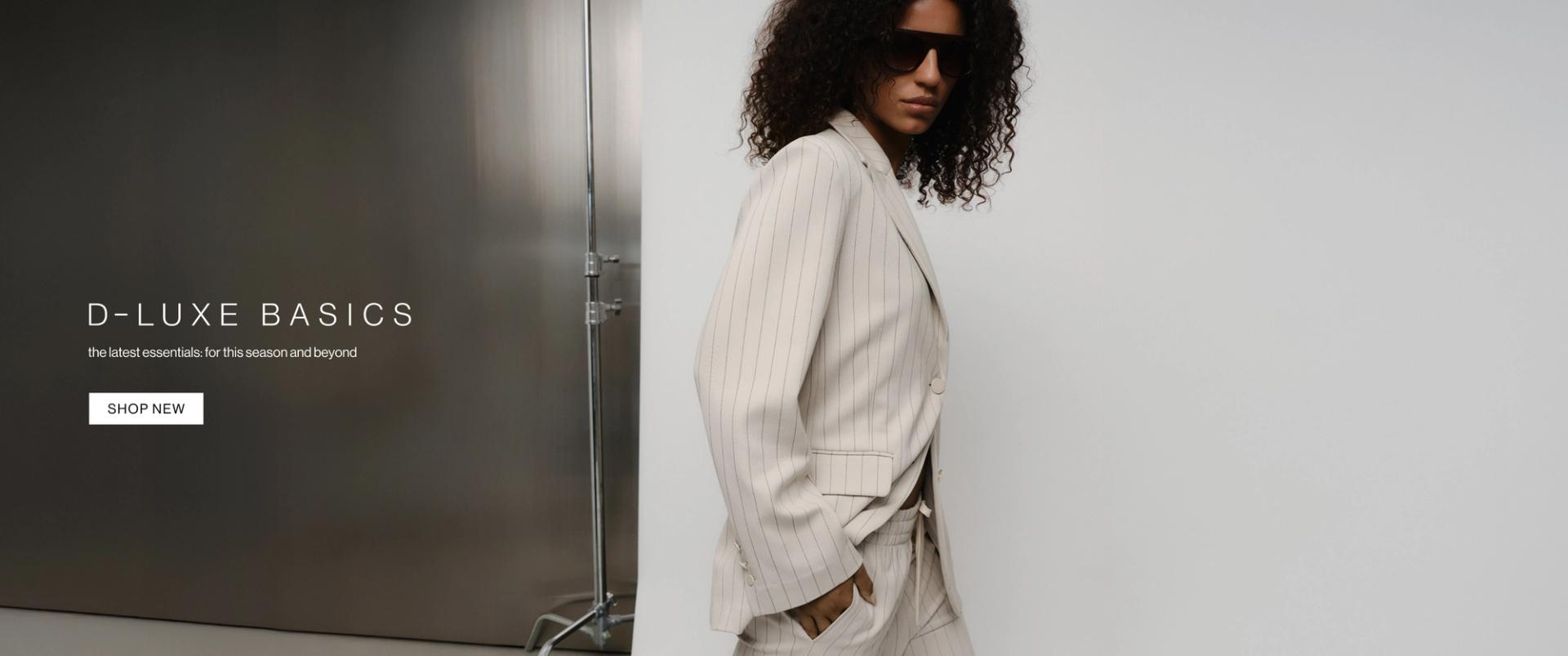 Model in a neutral pinstripe suit against a modern metallic wall with “D-Luxe Basics” headline.