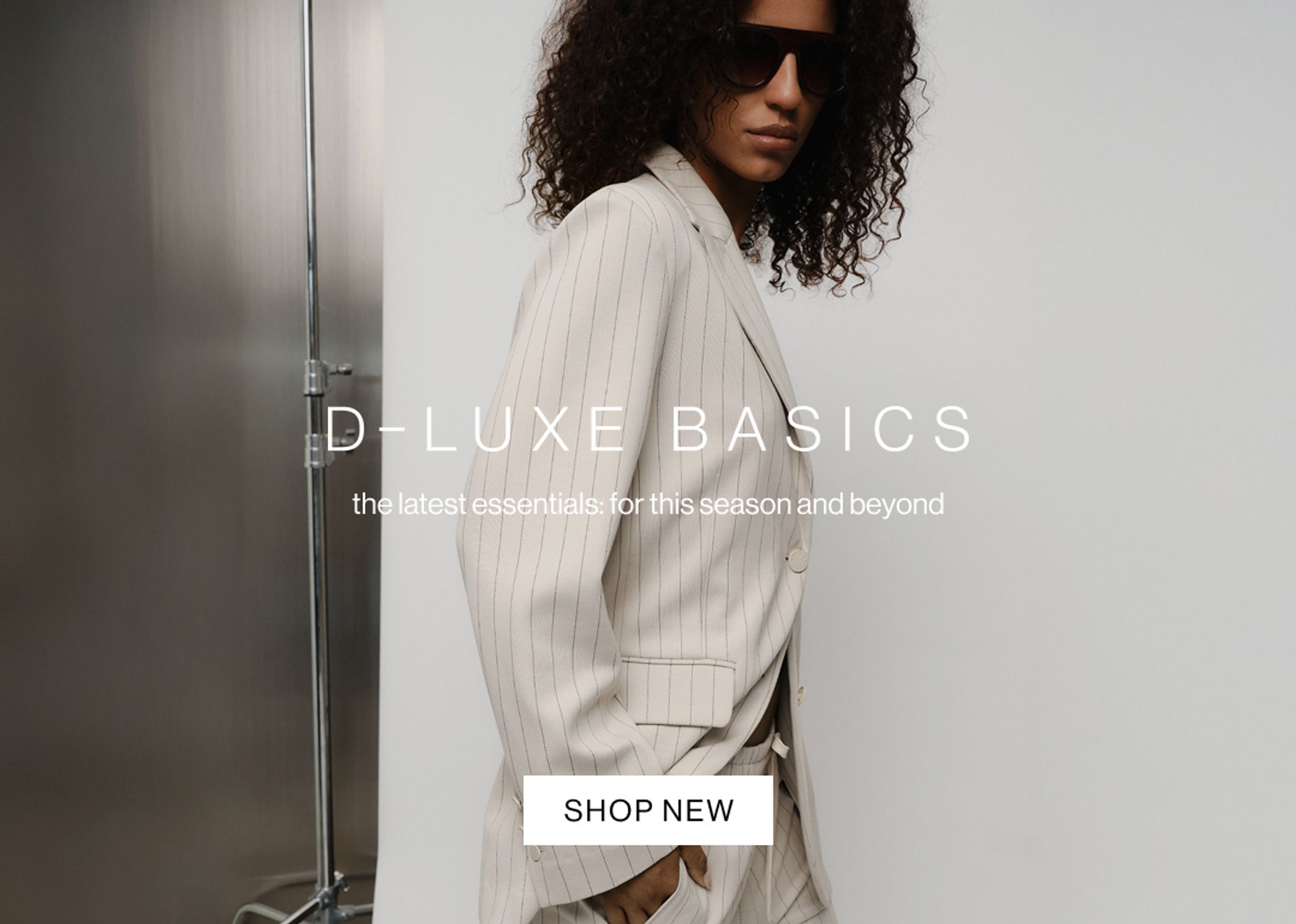 Model in a neutral pinstripe suit against a modern metallic wall with “D-Luxe Basics” headline.