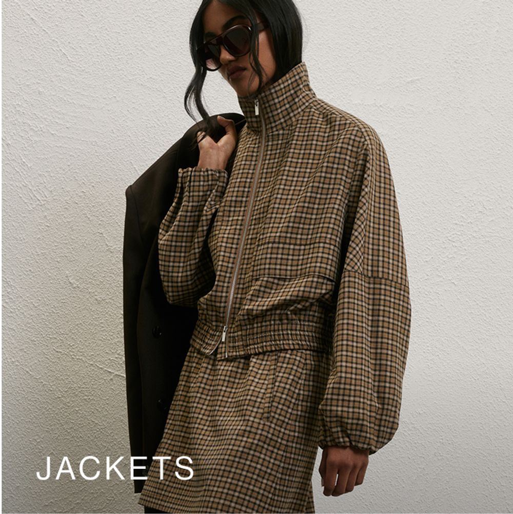 Model wearing a check print jacket and skirt. SHOP JACKETS.