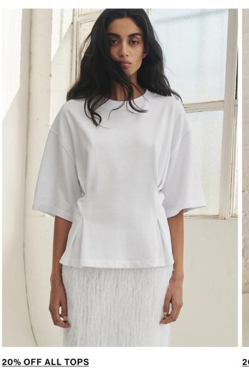 Model posing wearing a white tee. SHOP TOPS.