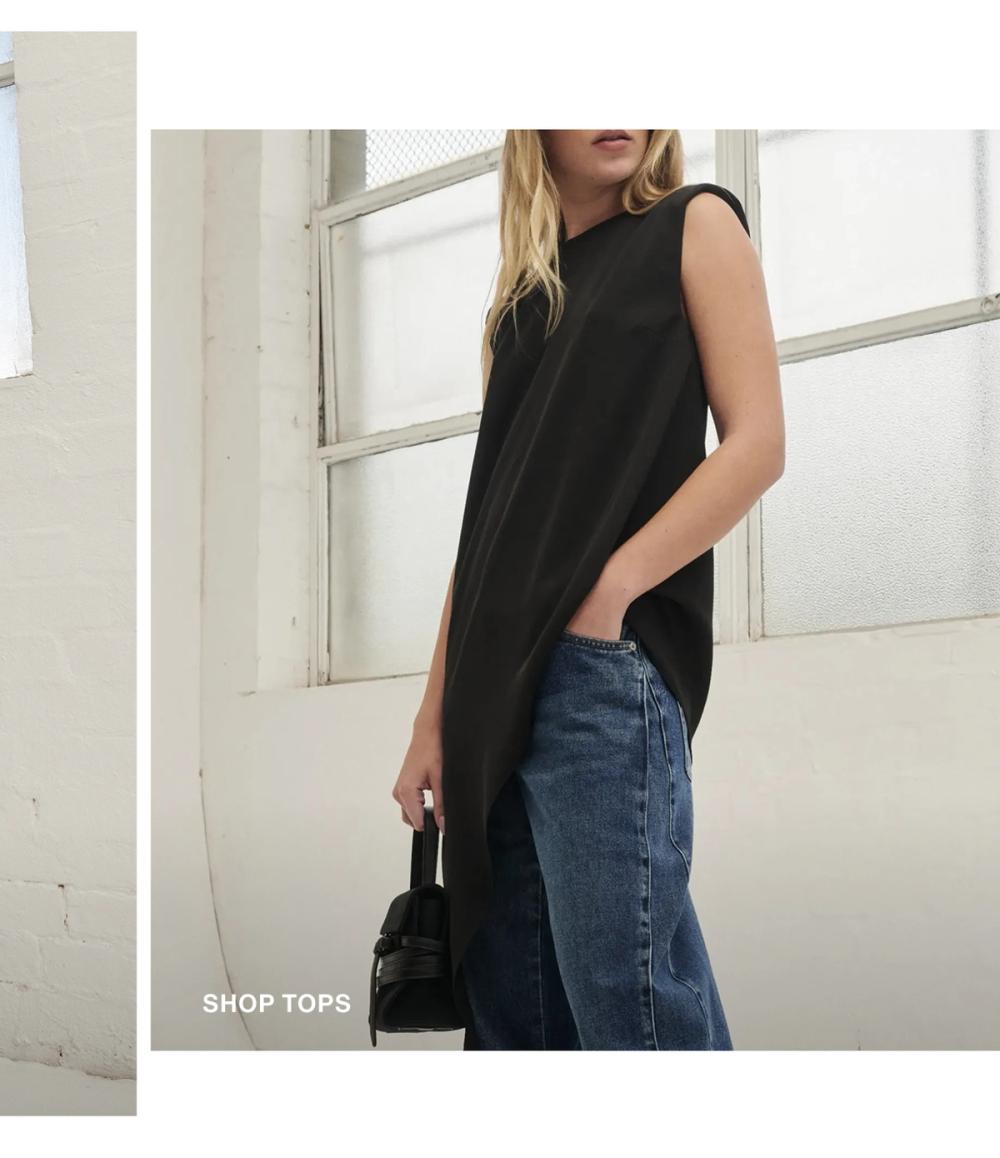 Model posing wearing a black side drape top. SHOP TOPS.