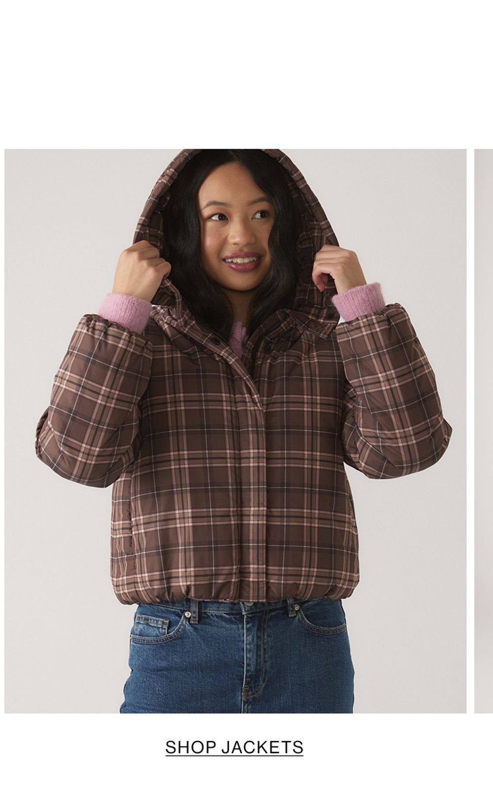 Young model wearing a brown and pink gingham pattern puffer jacket. SHOP TEEN GIRL JACKETS.