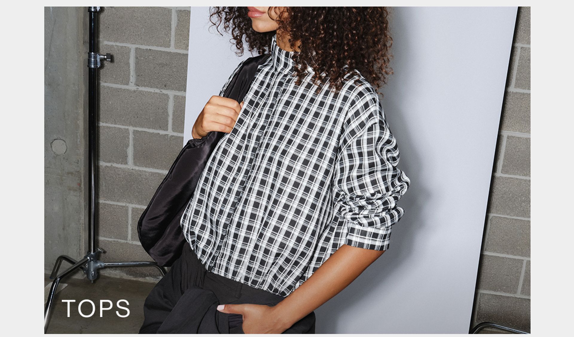 Model wearing a white and black check print shirt. SHOP D-LUXE TOPS.