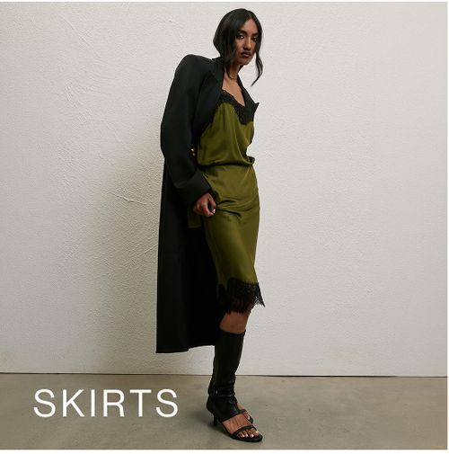 Model wearing a satin green skirt with black lace detailing. SHOP SKIRTS.