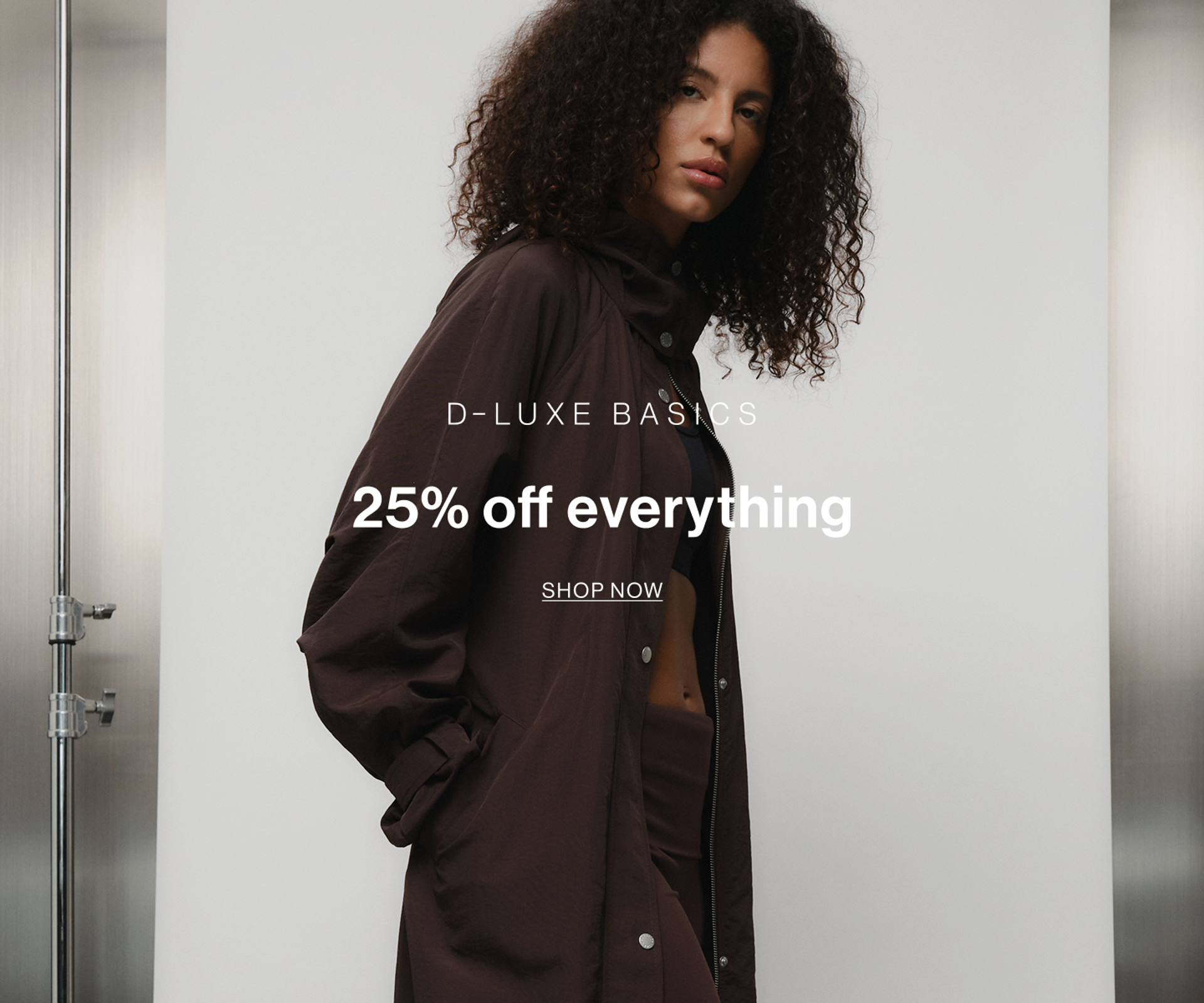 Model wearing brown shirt and trousers set, promoting D-Luxe Basics collection with 25% off.