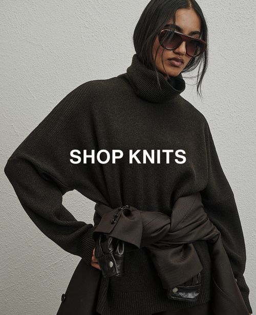 Woman in a blue knit in front of a white wall with text that reads "20% off all Knits"