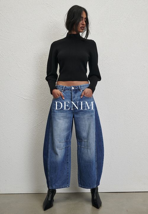 Woman posing in front of a white wall wearing a jeans and a black long sleeve top with text that states "denim"